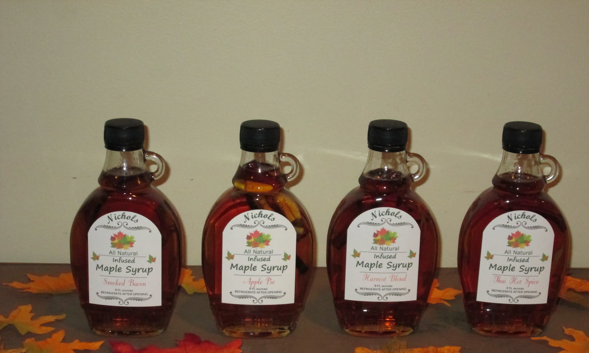 Four bottles of Nichols infused maple syrup on autumn leaves